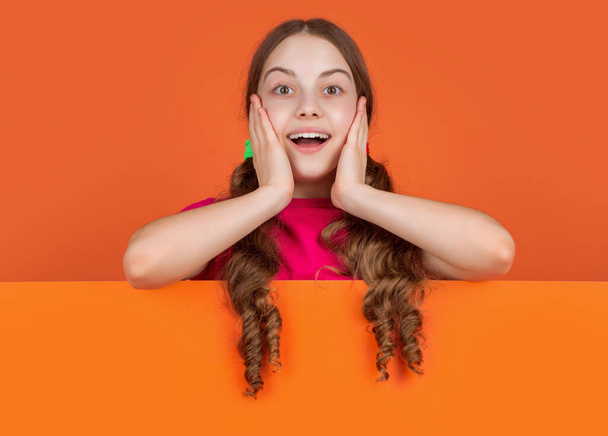 happy child behind blank orange paper with copy space for advertisement. wow. - Foto, imagen