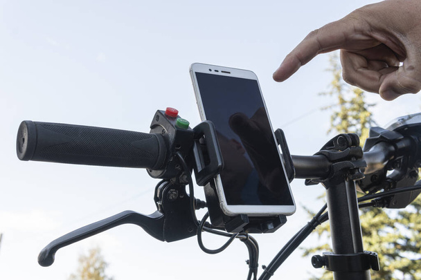 サイクリストの手はサイクリング中にスマートフォンのGPSナビゲーターを使います。男はスマートフォンの画面に指を押して. - 写真・画像