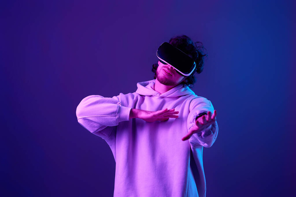 man in sweatshirt using virtual reality headset on blue background. Neon lighting - Foto, afbeelding