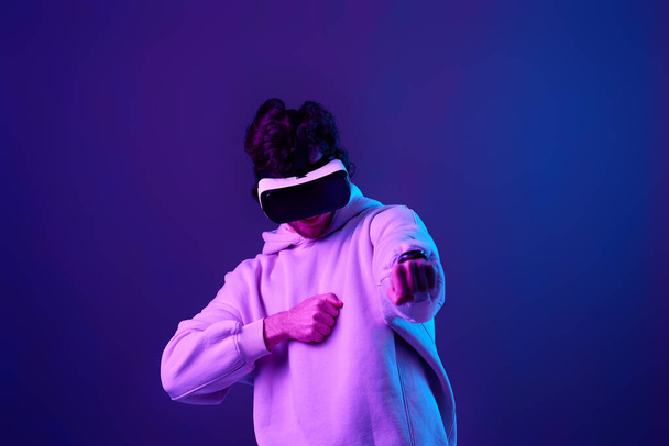 man in sweatshirt using virtual reality glasses on blue background. Neon lighting - Photo, image
