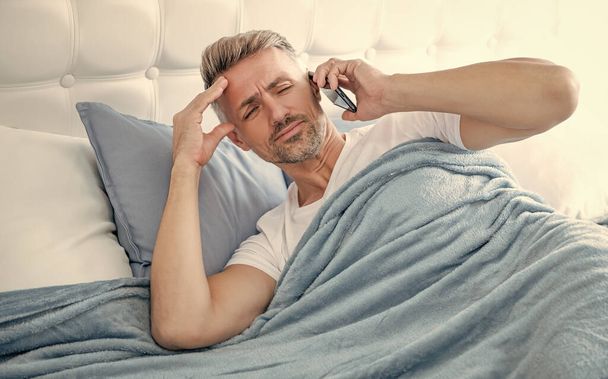 confused mature man in bed speaking on phone. - Zdjęcie, obraz