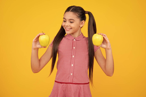 Child girl eating an apple over isolated yellow background. Tennager with fruit. Happy teenager, positive and smiling emotions of teen girl - Photo, Image