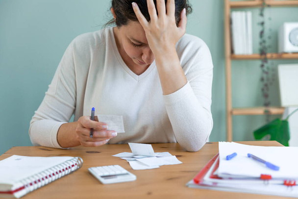 Sad depressed young woman holding bills, having problems with dismissal at home office. Expensive charges on domestic bills. Woman worried about financial problems. - Photo, Image