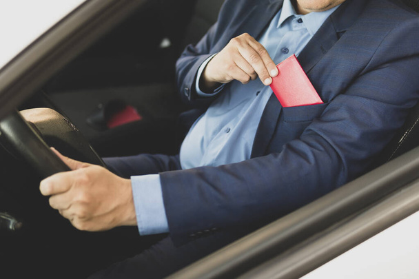 A rich businessman in a blue suit shows a red pass or document sitting in an expensive car. The politician holds an identity card in his hand. blank document for text and design. copy space - Photo, Image
