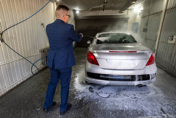 Homme laver la voiture avec une laveuse haute pression. Lavage de voiture avec mousse dans la station de lavage de voiture. Un homme pulvérise de la mousse sur la voiture à partir d'un spray spécial. - Photo, image