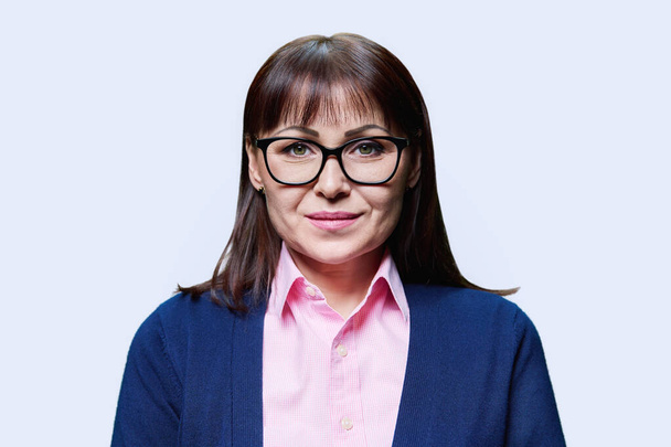 Close-up portrait of middle aged woman on white studio background. Smiling mature woman in glasses jacket looking at camera. Age people, profession, job, service, expertise concept - Zdjęcie, obraz
