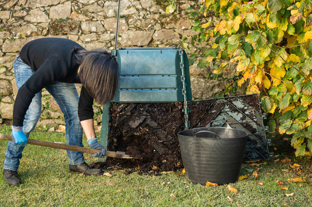 Egy férfi ásni és betölteni kész komposzt egy szabadtéri komposzt bin használni a kertben. A komposztálókosarat egy otthoni kertben helyezik el, hogy újrahasznosítsák az otthon és a kertben keletkező szerves hulladékot. Az újrafeldolgozás és a fenntarthatóság fogalma - Fotó, kép