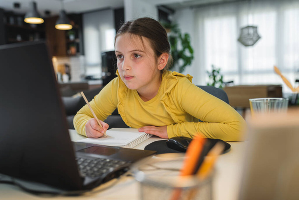 Söpö lapsi kuulokkeilla kannettavan tietokoneen avulla verkko-oppimiseen. Kotikoulu. Tyttö tekee läksyjä kotona. Kotikoulun elämäntapakonsepti. Sosiaalinen etäisyys ja koulutus. - Valokuva, kuva