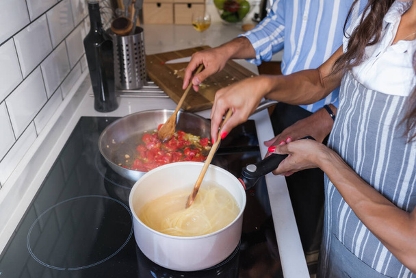 Gelukkig multi-etnisch paar koken zelfgemaakte tomaten en basilicum pasta. Koken thuis - Foto, afbeelding