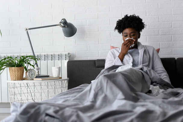 Young African-American woman lying in bed at home. Feeling ill having flu or coronavirus - Fotoğraf, Görsel