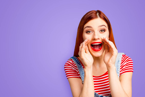 Portrait of nice vivid girlish red straight-haired happy young girl with opened mouth, announcing big sale, isolated over blue background, copy space. - Fotó, kép