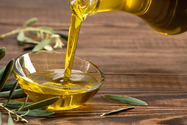 Organiczna oliwa z oliwek wlewająca się z karafki do szklanej miski - Zdjęcie, obraz