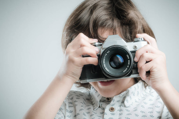 Niño con camisa blanca y detalles azules tomando fotos con cámara antigua. - Foto, Imagen