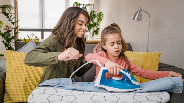 mother teaching her daughter to iron clothes - Foto, afbeelding