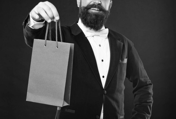cropped smiling man in tuxedo bow tie formalwear on black background presenting shopping bag. birthday. copy space. - Fotoğraf, Görsel