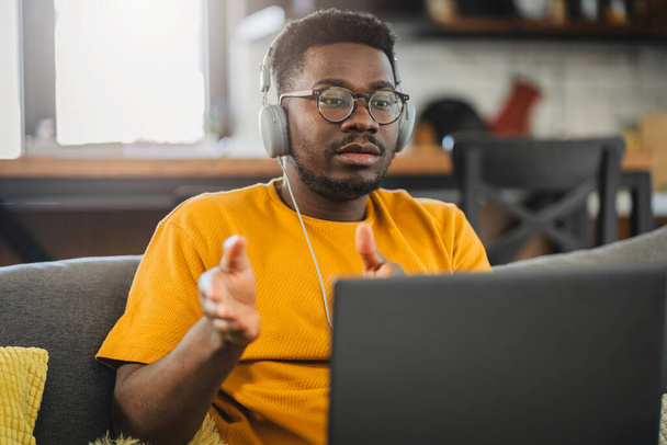 Jovem estudante afro-americano em casa, ouvindo aulas on-line, ou um webinar sobre um computador portátil - Foto, Imagem