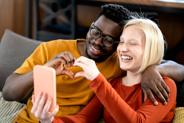 幸せな多民族のカップルが屋内でスマートフォンで何かを見て - 写真・画像