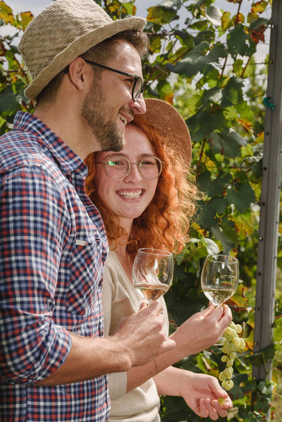 Fiatal mosolygós pár kóstoló bor pincészet szőlő - Barátság és szerelem koncepció a fiatalok élvezik a betakarítás ideje - Fotó, kép