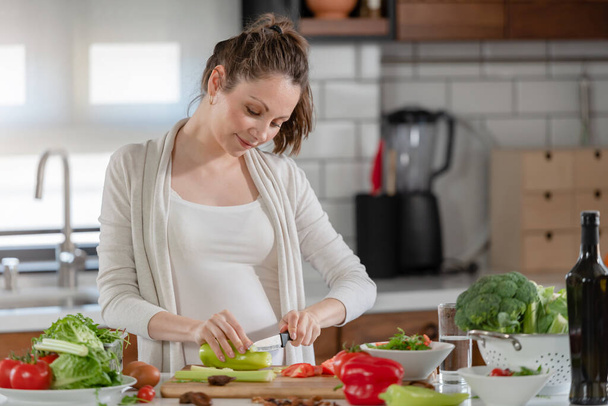 Молодая беременная женщина готовит здоровую пищу из фруктов и овощей - Фото, изображение