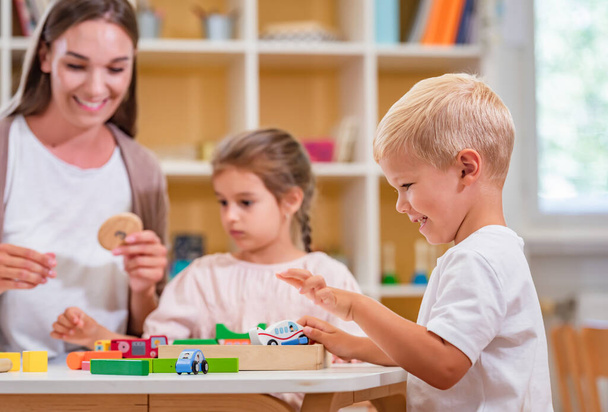 Kindergarten teacher playing together with children at colorful preschool classroom. Mother playing with children. - Photo, Image