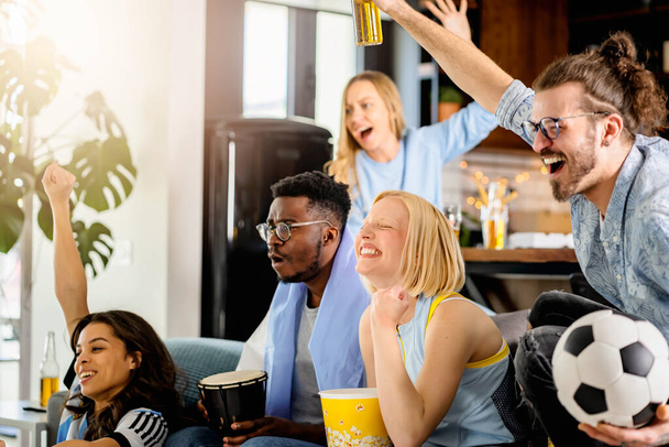 Aufgeregte Gruppe junger multiethnischer Menschen, die zu Hause am Fernseher ein Fußballspiel verfolgen - Foto, Bild