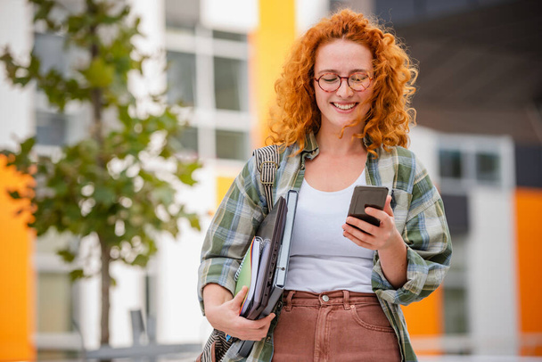 Ritratto di una bella studentessa dai capelli rossi sorridenti con telefono - Foto, immagini