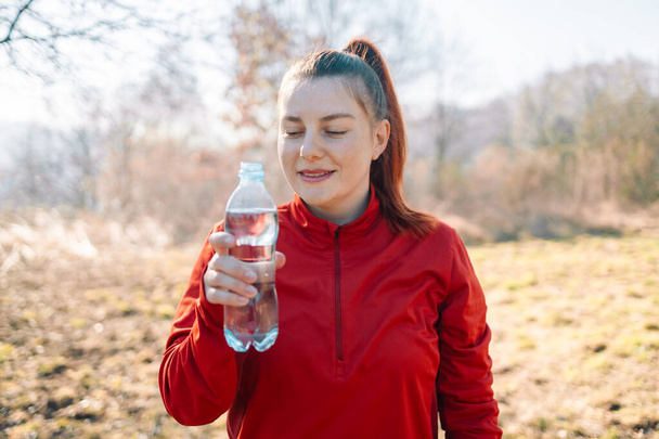 Image of sportswoman drinking water while working out on sports ground - Valokuva, kuva