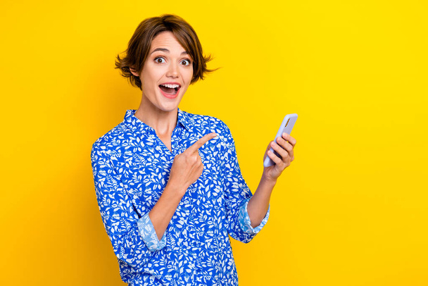 Photo of funky excited woman dressed blue blouse pointing finger modern device empty space isolated yellow color background. - Foto, afbeelding