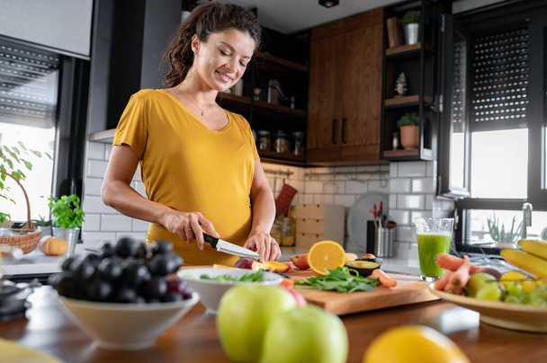 妊娠中の女性が台所で料理をしたり健康的な食事をしたり - 写真・画像