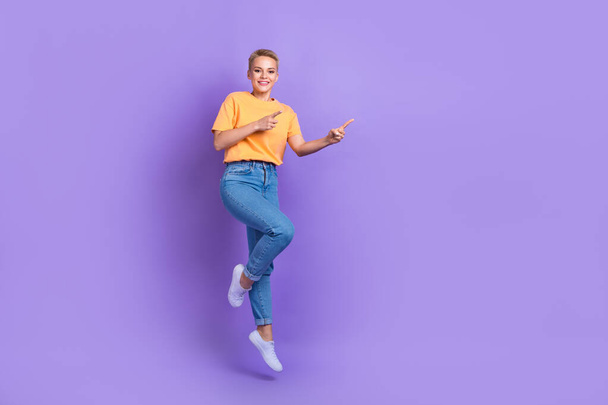 Full length photo of positive nice girl dressed white sneakers jeans pants directing empty space isolated on violet color background. - Photo, image