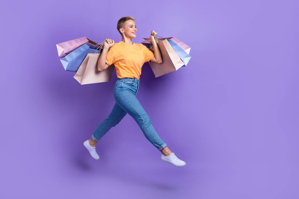 Full length profile portrait of carefree active person hold boutique bags jump run empty space isolated on purple color background. - Φωτογραφία, εικόνα