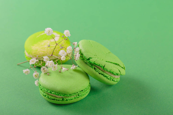 Green monochrom food background with french macaroons and flowers with copy space for text. Close up of macarons cakes. Culinary and cooking concept - Foto, Imagem
