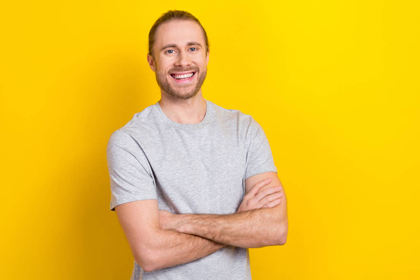 Zdjęcie pozytywne pewny siebie mężczyzna nosić szary t-shirt uśmiechnięte ramiona skrzyżowane odizolowany żółty kolor tła. - Zdjęcie, obraz