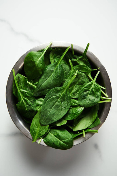 A bunch of Fresh baby spinach leaves in the in a stainless steel bowl on white marble background. High quality photo - 写真・画像