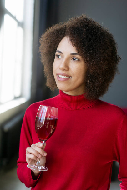 Kaunis Afrikkalainen amerikkalainen nuori nainen rento vaatteita, tilalla viinilasi makuista herkullista punaviiniä, etsivät luottavaisesti sivuun. Juomateollisuus. Juomaa. sommelieri - Valokuva, kuva