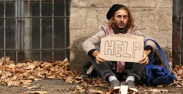 Köyhä koditon mies pitelee pahvia tekstillä HELP ulkona
 - Valokuva, kuva