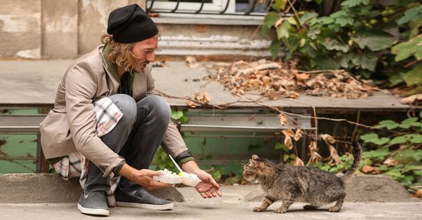 Poor man sharing food with homeless cat outdoors - Photo, Image