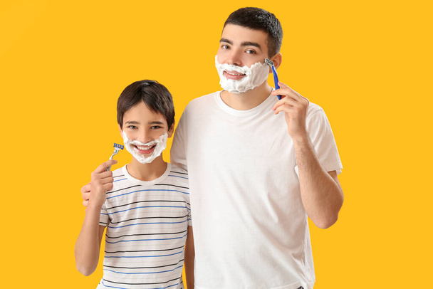 Man and his little son shaving against yellow background - Foto, imagen
