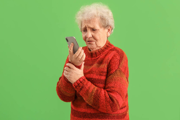 Smutná starší žena s mobilním telefonem na zeleném pozadí - Fotografie, Obrázek