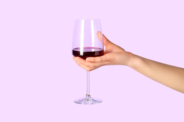 Female hand holding glass of red wine on lilac background - Photo, Image