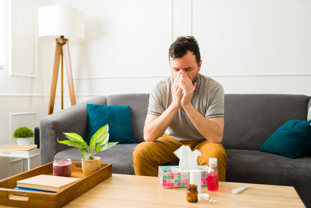 Sick caucasian man blowing his nose with tissues suffering from a cold while taking medicines at home - Valokuva, kuva