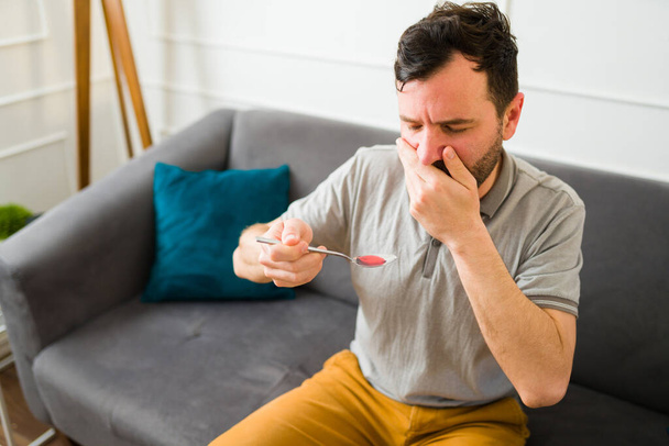 Worried caucasian man in his 30s covering his mouth before taking coughing syrup to recover from a cold - Foto, immagini
