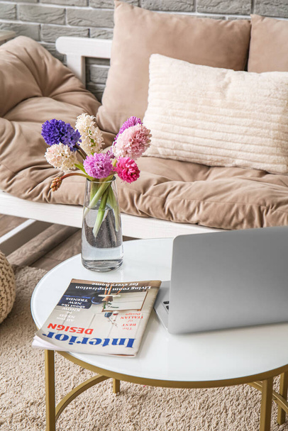 Moderno portátil, jarrón con flores de jacinto y revista en la mesa de café en la sala de estar - Foto, imagen
