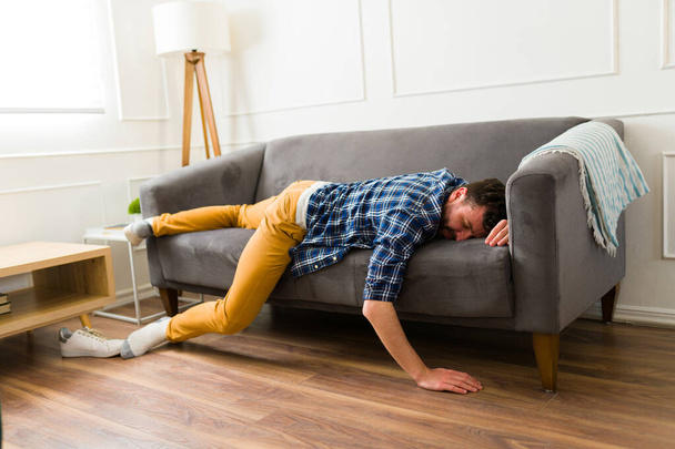 Втомлений серед дорослий чоловік відчуває себе виснаженим і відпочиває на животі на дивані під час сну у вітальні
 - Фото, зображення