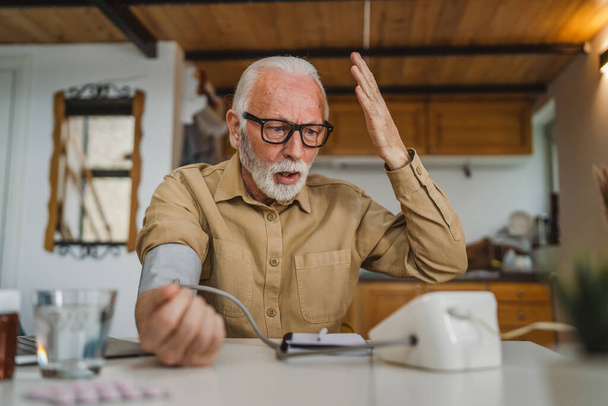 Один чоловік старший кавказький чоловік з бородою використовує пристрій кров'яного тиску, щоб перевірити і виміряти результати, сидячи за столом вдома тільки реальні люди копіюють концепцію охорони здоров'я читати погані результати
 - Фото, зображення