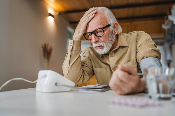 Один чоловік старший кавказький чоловік з бородою використовує пристрій кров'яного тиску, щоб перевірити і виміряти результати, сидячи за столом вдома тільки реальні люди копіюють концепцію охорони здоров'я читати погані результати
 - Фото, зображення