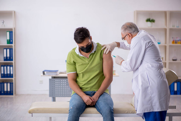 Jeune patient visitant un vieux médecin dans le concept de vaccination - Photo, image