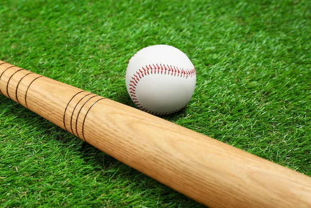 Wooden baseball bat and ball on green grass, closeup. Sports equipment - 写真・画像