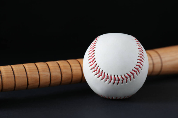 Wooden baseball bat and ball on black background, closeup. Sports equipment - Zdjęcie, obraz