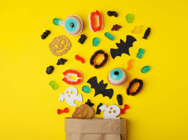 Paper bag of tasty candies and Halloween decorations on yellow background, flat lay - Zdjęcie, obraz